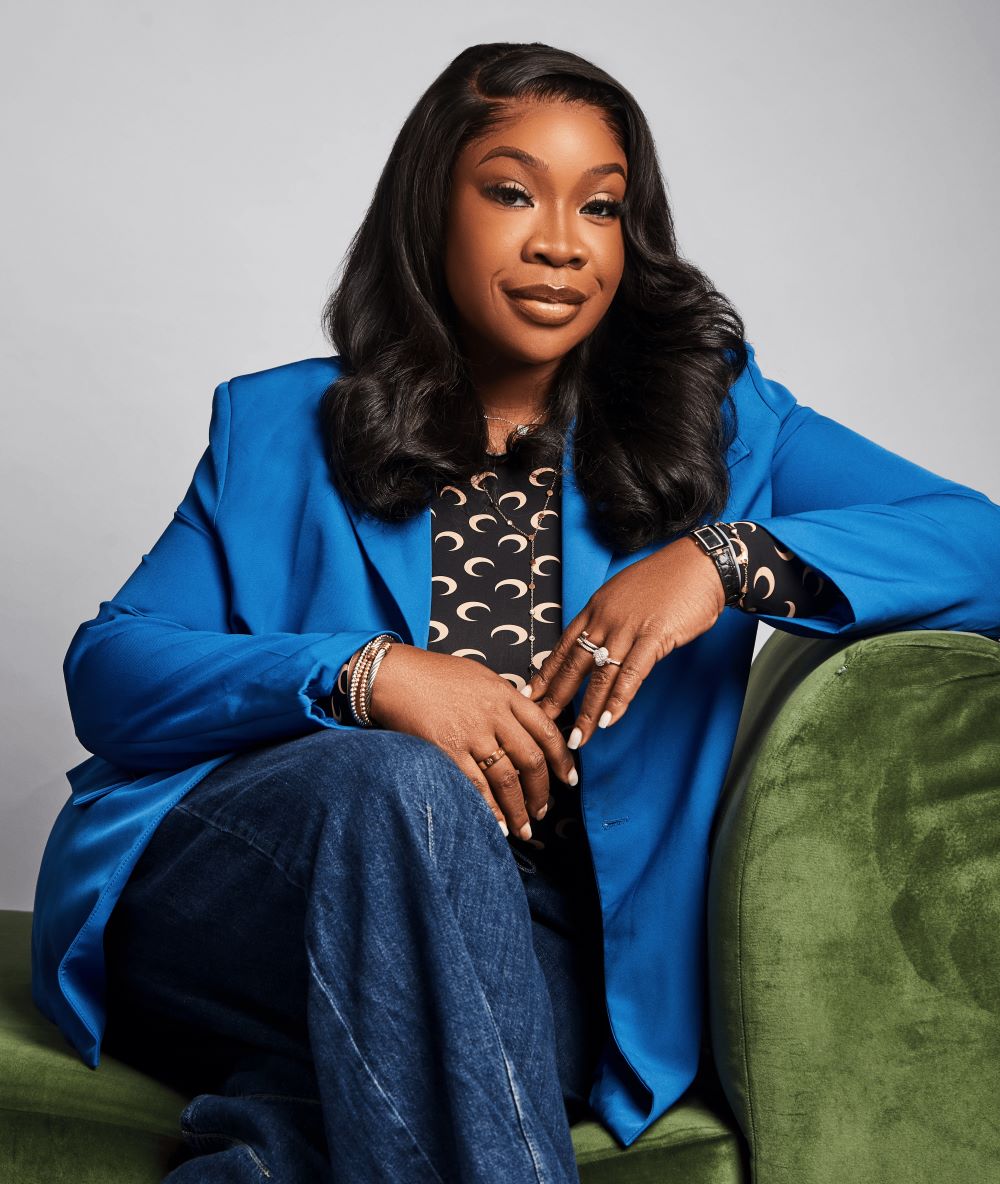 Dr. Bukky George-Taylor seated on a green velvet chair, in a royal-blue blazer over a crescent-print top.