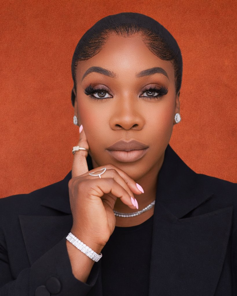Portrait of Dr. Bukky George-Taylor in a black blazer and diamond jewellery, chin resting on her hand, against a terracotta backdrop.